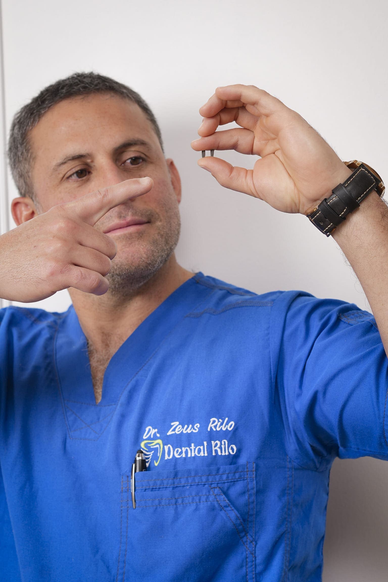 Dr. Zeus Rilo en uniforme clínico explicando un implante dental con modelo educativo